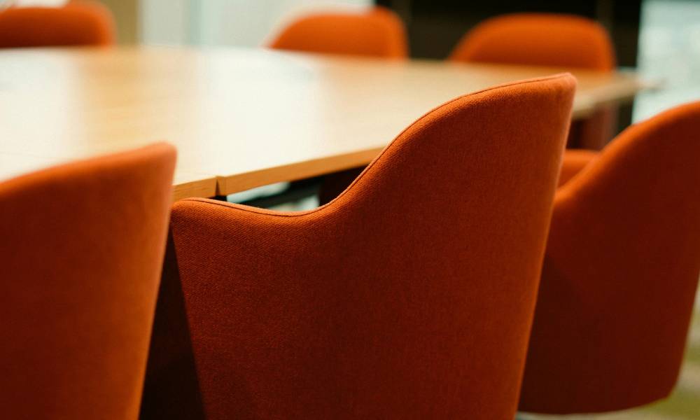 Oranssin värisiä kangasverhoiltuja tuoleja puupintaisen pöydän ympärillä.