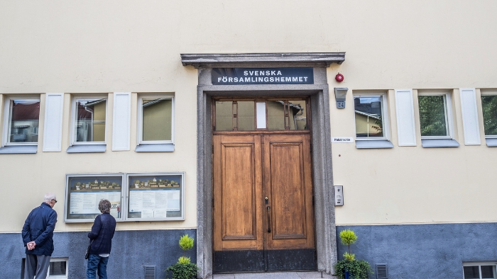 Runeberginkadun seurakuntakodin ulko-ovi ja kaksi henkilöä sen vieressä katsomassa ilmoitustaulua.