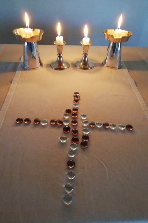 lasihelmistä muodostettu risti ja neljä palavaa kynttilää.