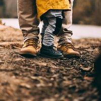 Aikuisen ja lapsen jalat ulkokengissä ruskealla maalla